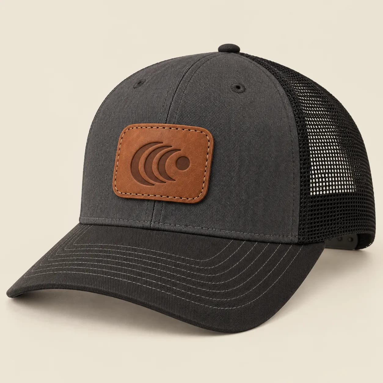 Custom Leather Patch Trucker Hats: Charcoal trucker hat with black mesh, a tan rectangular stitched leather patch and a dark curved sample logo