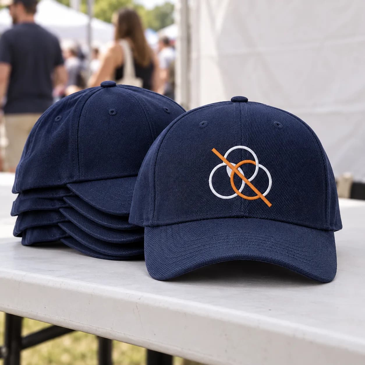 Custom 6-Panel Baseball Hats: A stack of embroidered 6 panel caps on a merch table at an outdoor event